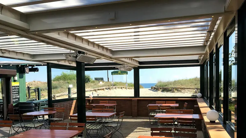 Innenansicht - Restaurantterrasse mit Lamellendach und seitlicher verschiebbarer Verglasung als  Wind- und Wetterschutz.