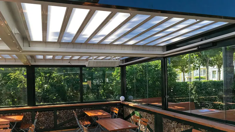 Innenansicht - Restaurantterrasse mit Lamellendach und seitlicher verschiebbarer Verglasung als  Wind- und Wetterschutz.