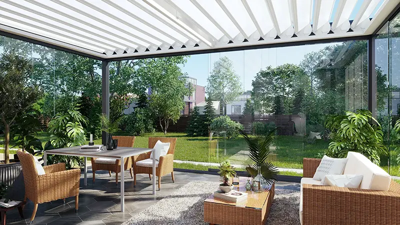 Innenbereich eines FLEDMEX<sup>®</sup> Lamellendachs mit teilweise geöffneten Ganz-Glas-Schiebeanlagen, gemütlicher Sitzgruppe und üppiger Bepflanzung mit Blick in den Garten.